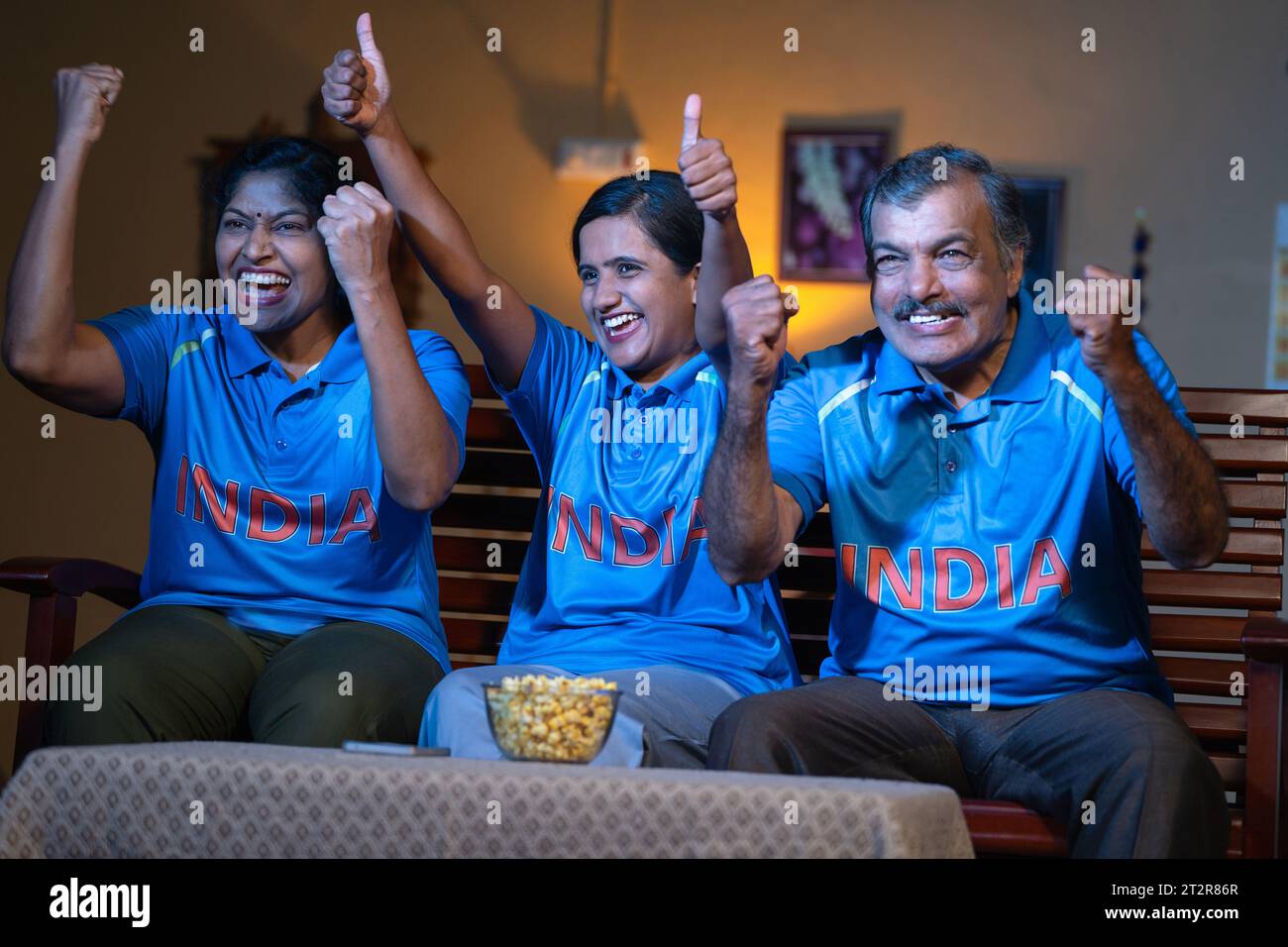 excited family celebrating victory of Cricket Team in Indian jersey, watching on tv or television at home - concept of World cup match, championship Stock Photo