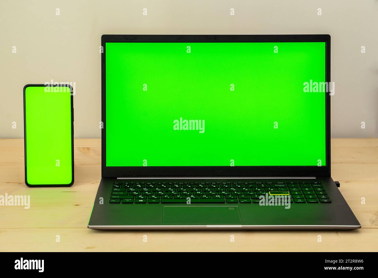 Photo of laptop and smartphone on wooden desk showing green screen. Stock Photo