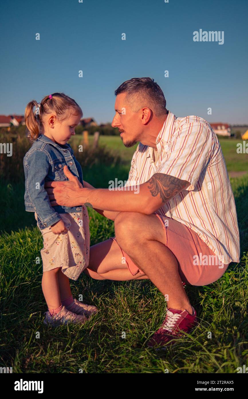 Dad and daughter of Caucasian appearance walking in a meadow on a summer sunny day at sunset. A man with his daughter spends time playing in nature. Stock Photo