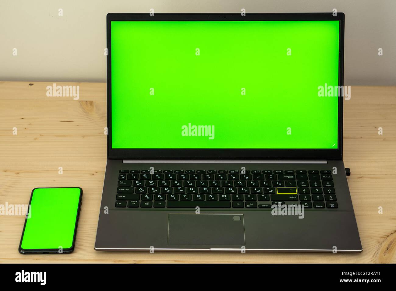 Photo of laptop and smartphone on wooden desk showing green screen. Stock Photo