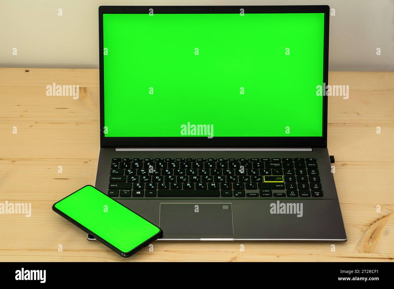 Photo of laptop and smartphone on wooden desk showing green screen. Stock Photo