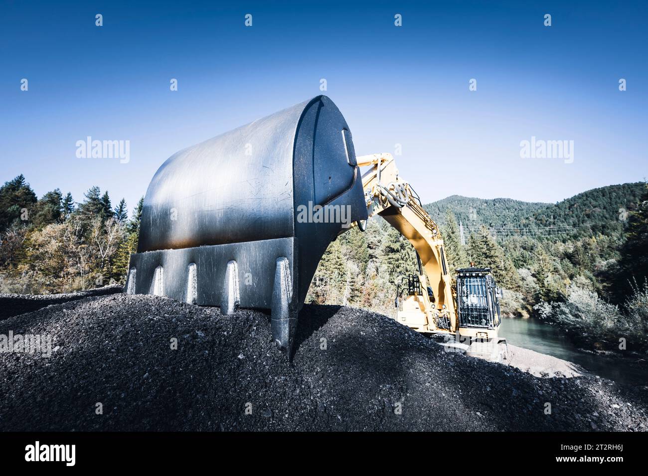 Large tracked excavator bucket in fine gravel in wooded nature with blue sky Stock Photo