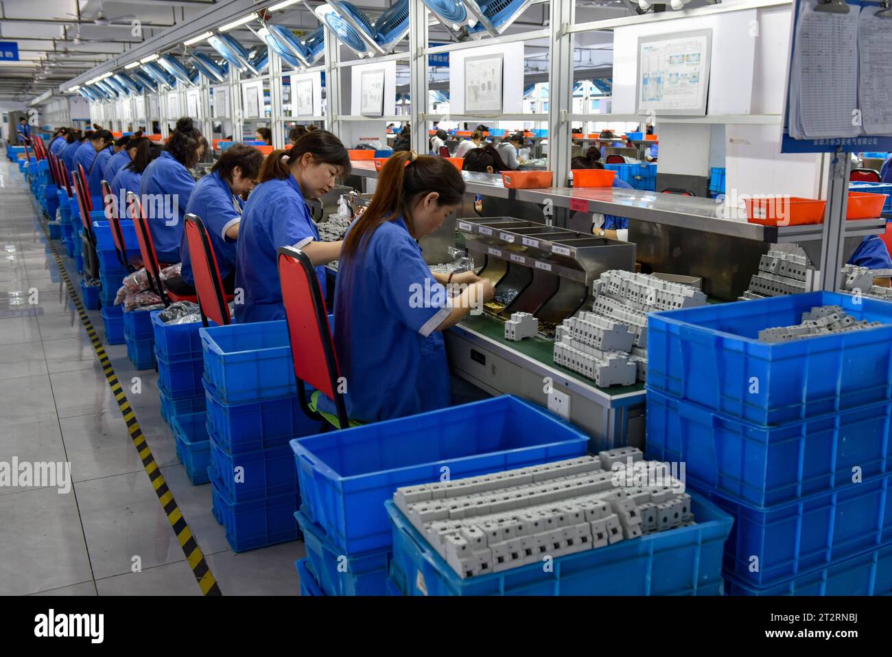 Women wearing blue overalls work on the assembly line of a factory that ...