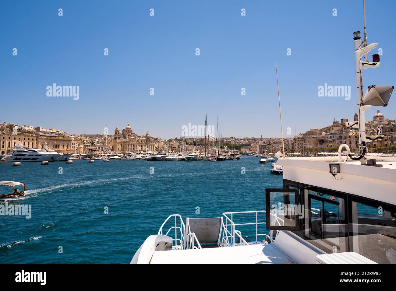 Vittoriosa, Malta - 17 June 2023: Vittoriosa harbor with yachts and boats and the dome of the cathedral in the background, taken from board the ferry Stock Photo
