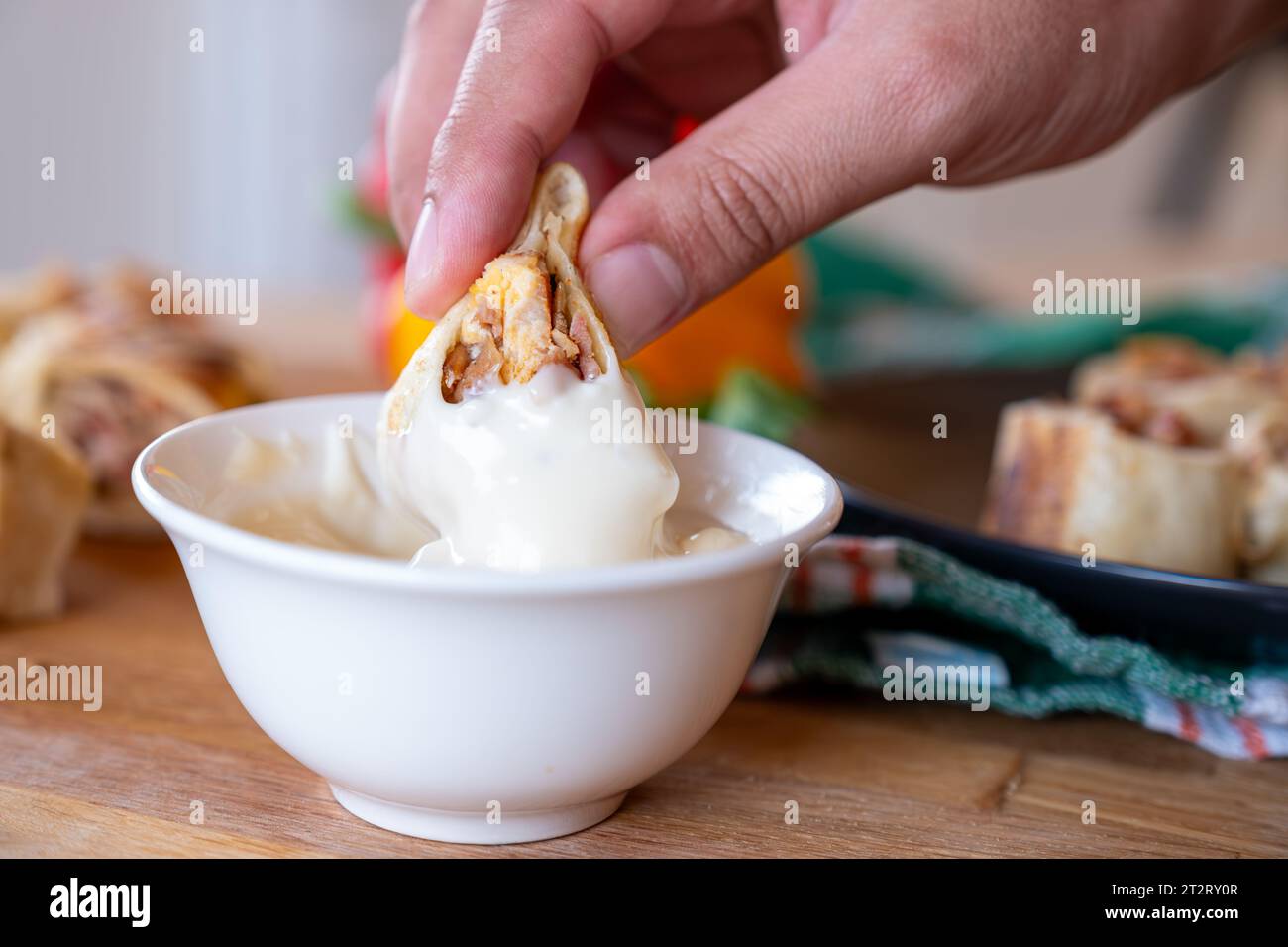 hand holding shawarma piece and dip it in mayonnaise or garlic tahini
