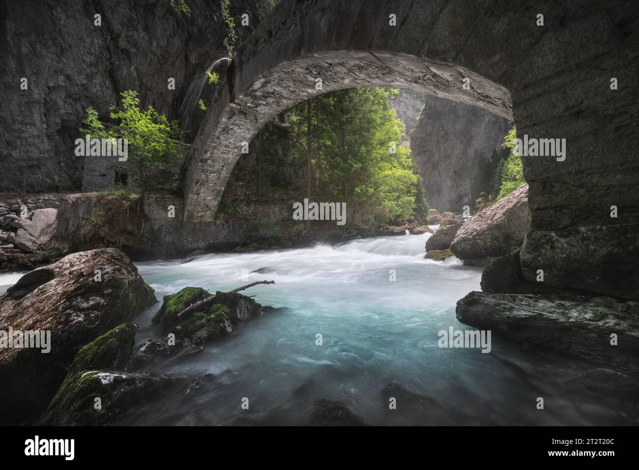 An old stone bridge over the stream in the Orrido of Pré Saint Didier, a view in summer of this deep ravine in Aosta valley. Italy. Stock Photo