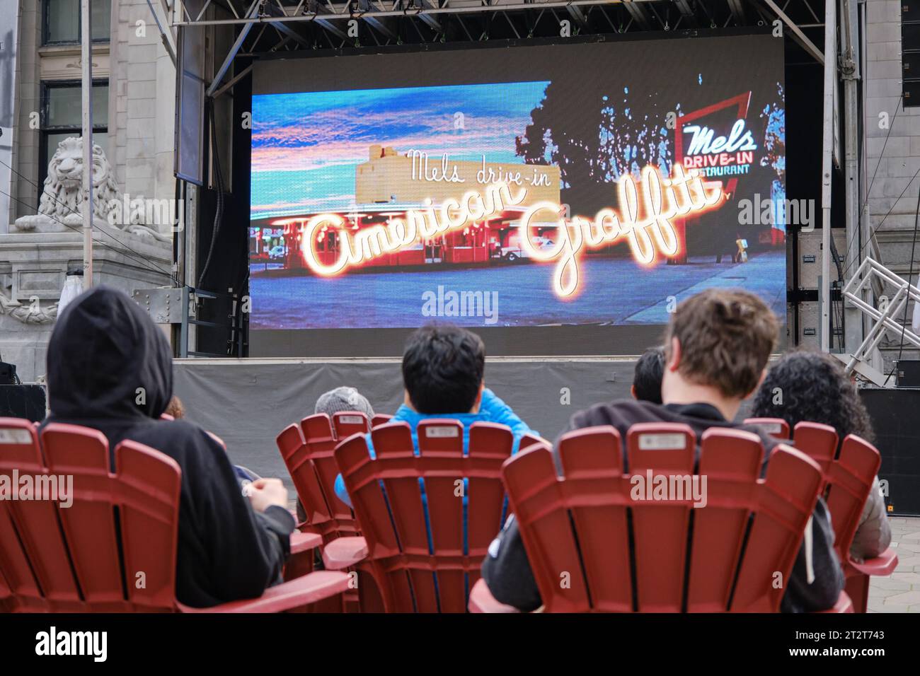 outdoor film projection of American Graffiti with people sitting on plastic Adirondack chairs Stock Photo