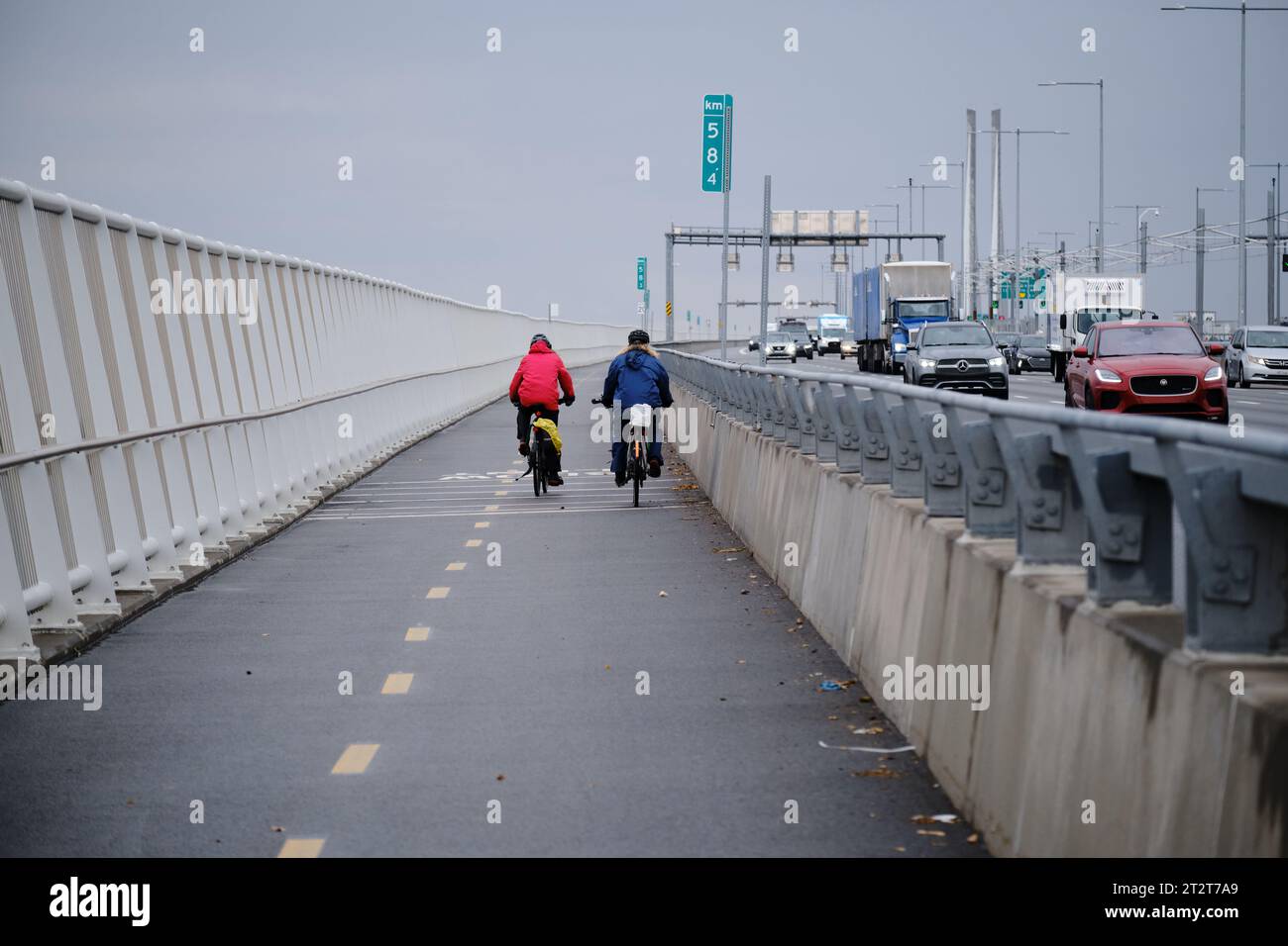 two cyclists seen from behind using the reserved bike lane on Champlain Bridge in Montreal, while car go by Stock Photo