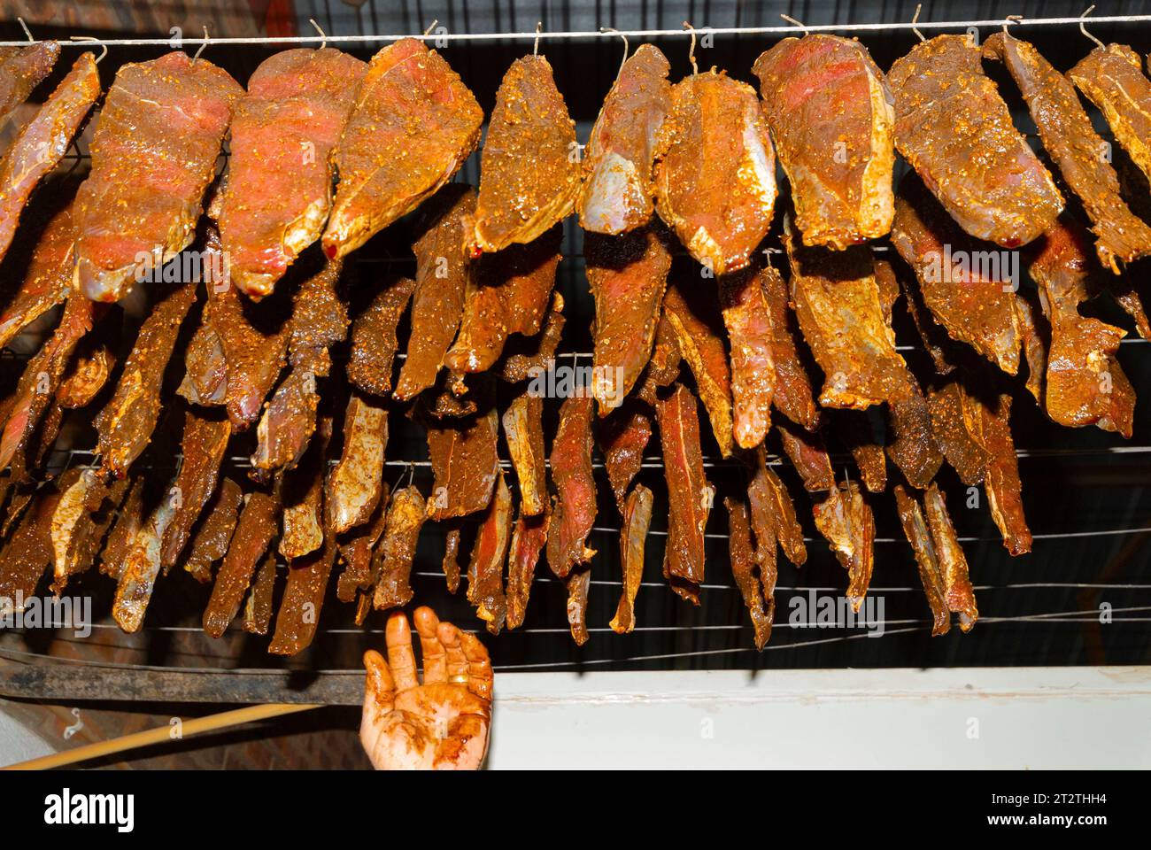 Large cuts of meat covered in spices hang from a set of hooks to dry