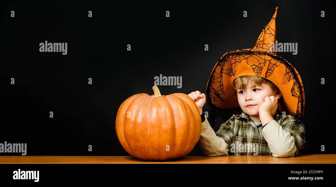 Happy Halloween. Cute child boy in witch hat with Halloween pumpkin. Little kid wizard with Jack-o-lantern preparing for Halloween holidays. Halloween Stock Photo