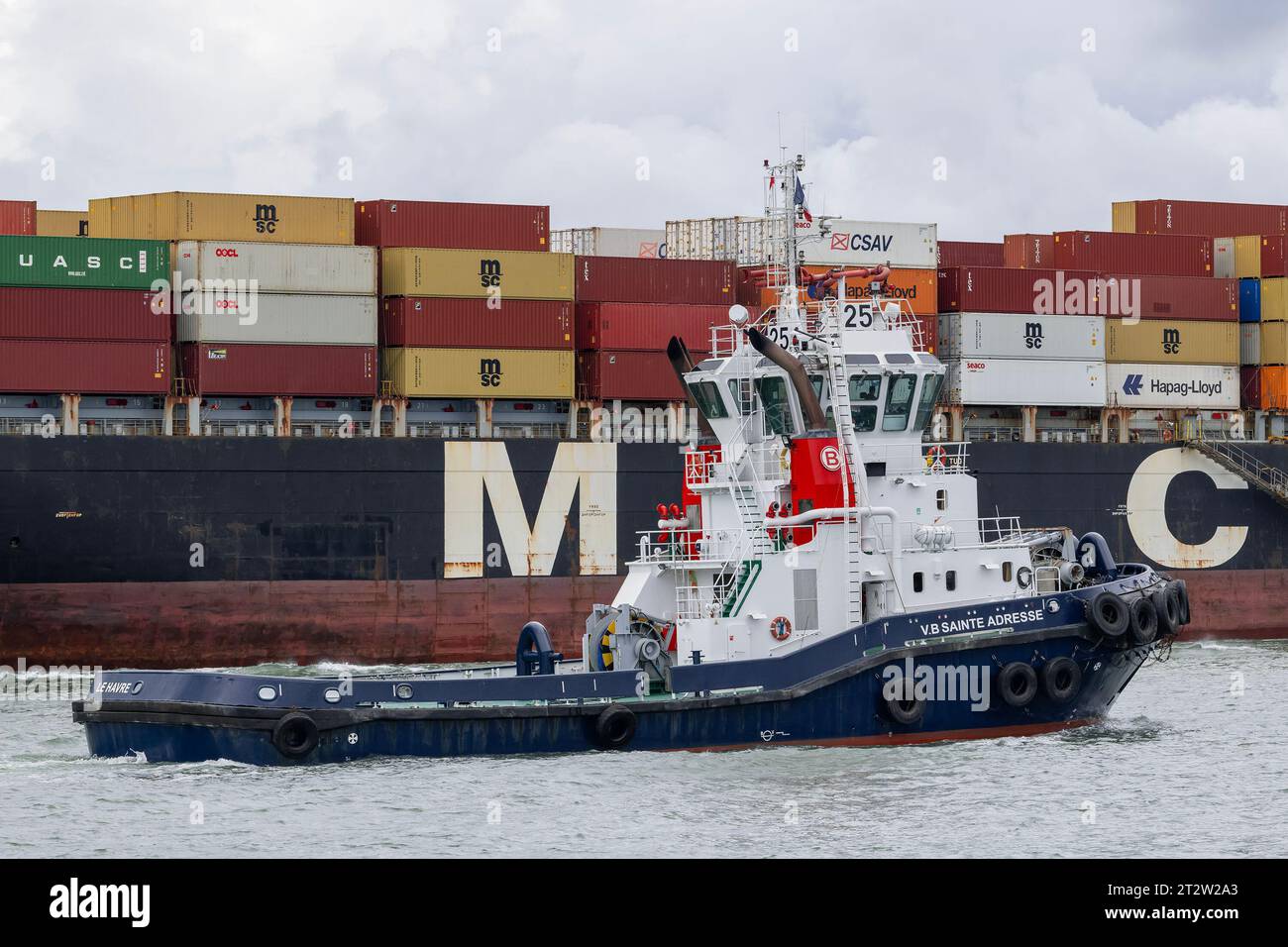 Le Havre, France - Harbour tug VB SAINTE ADRESSE crosses in front of a container ship at port of Le Havre. Stock Photo