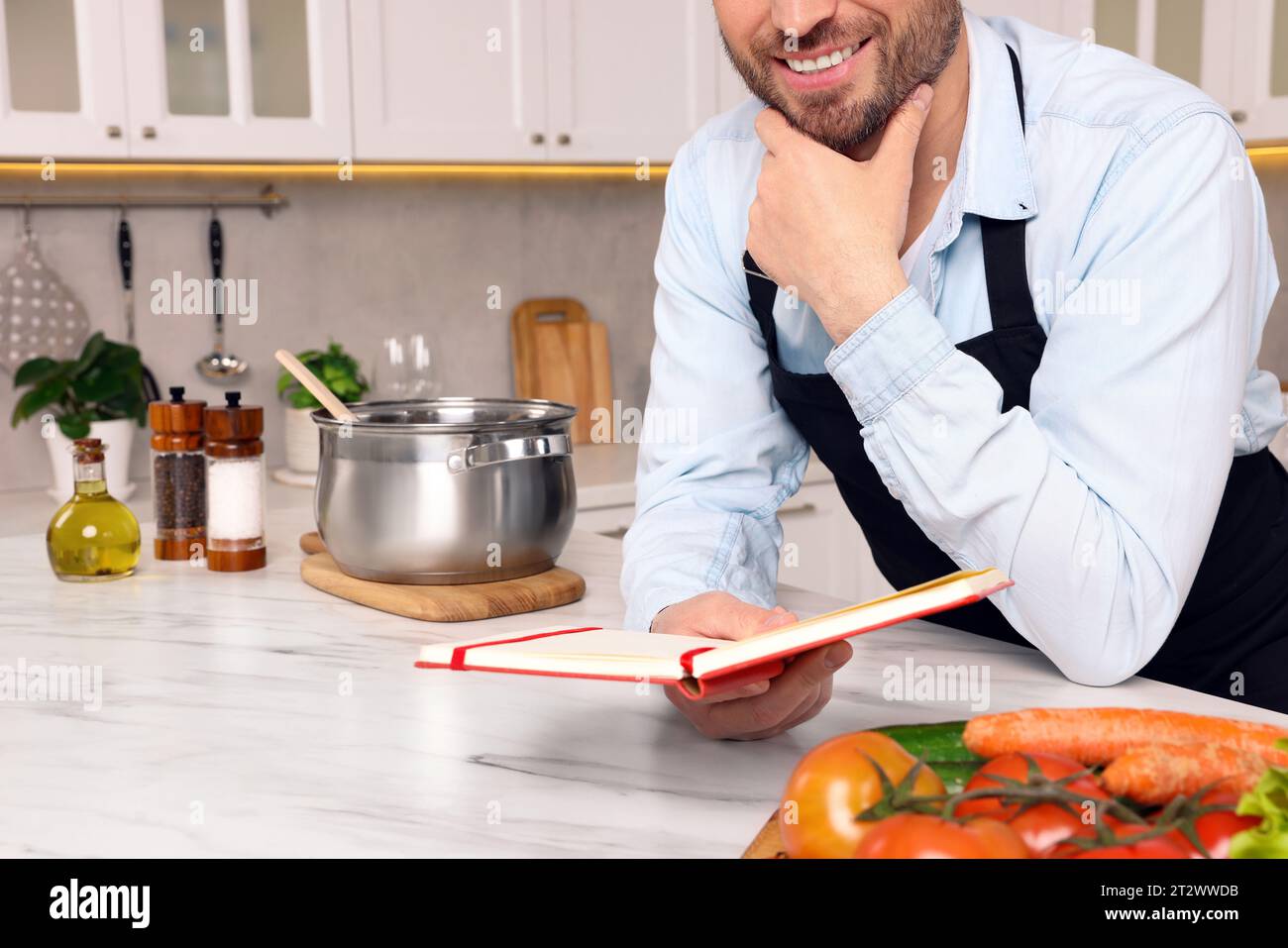Man with recipe book at white marble table in kitchen, closeup Stock Photo