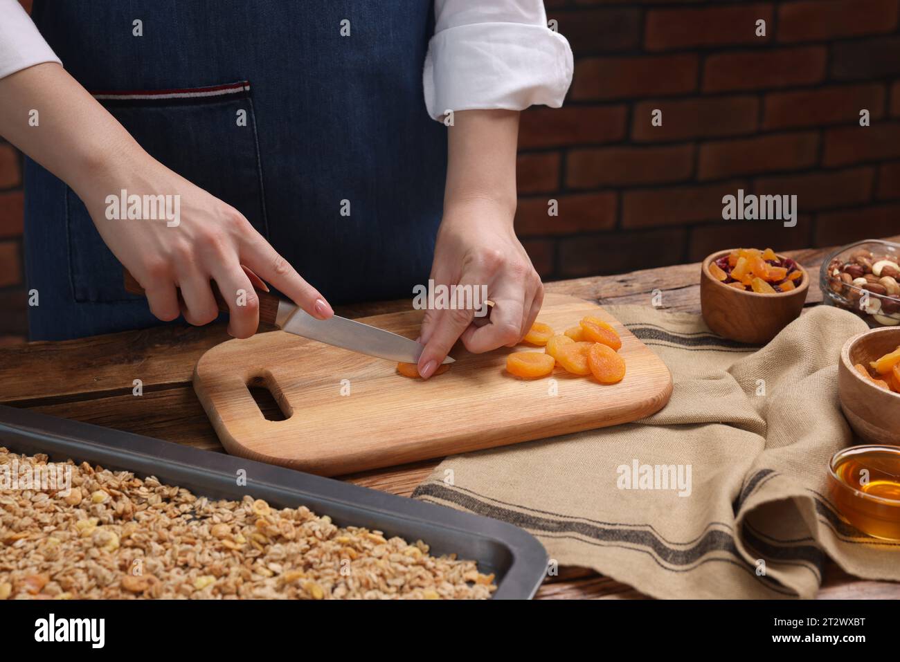 Making granola. Woman cutting dry apricots at wooden table, closeup