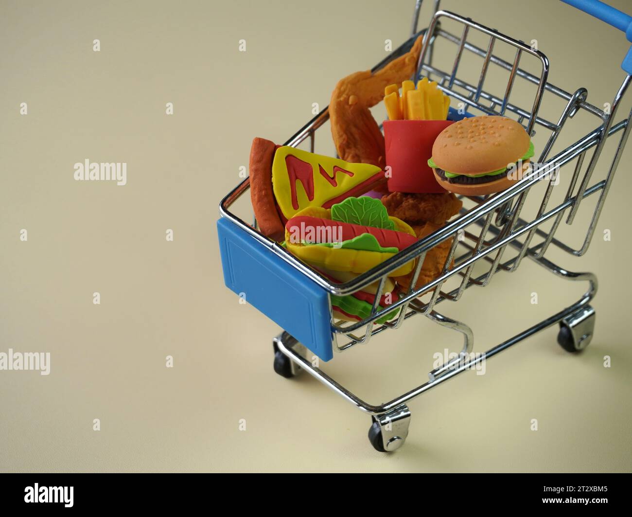Closeup image of shopping cart full with junk foods like burger, fries and pizza. Copy space for text. Bad eating habits concept. Stock Photo
