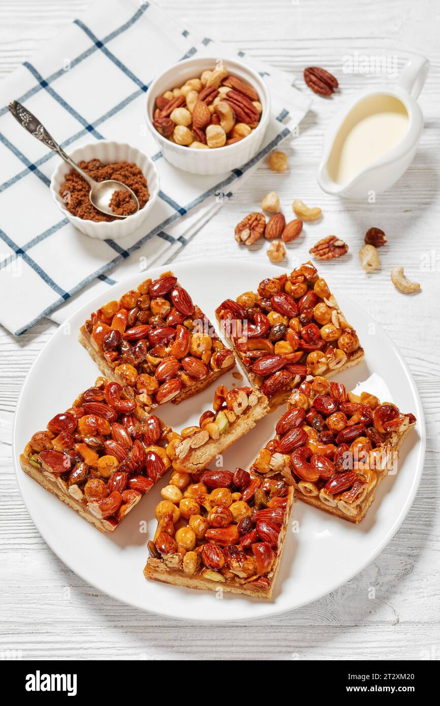 homemade toffee mixed nuts shortbread bars on white plate on white wooden table with ingredients
