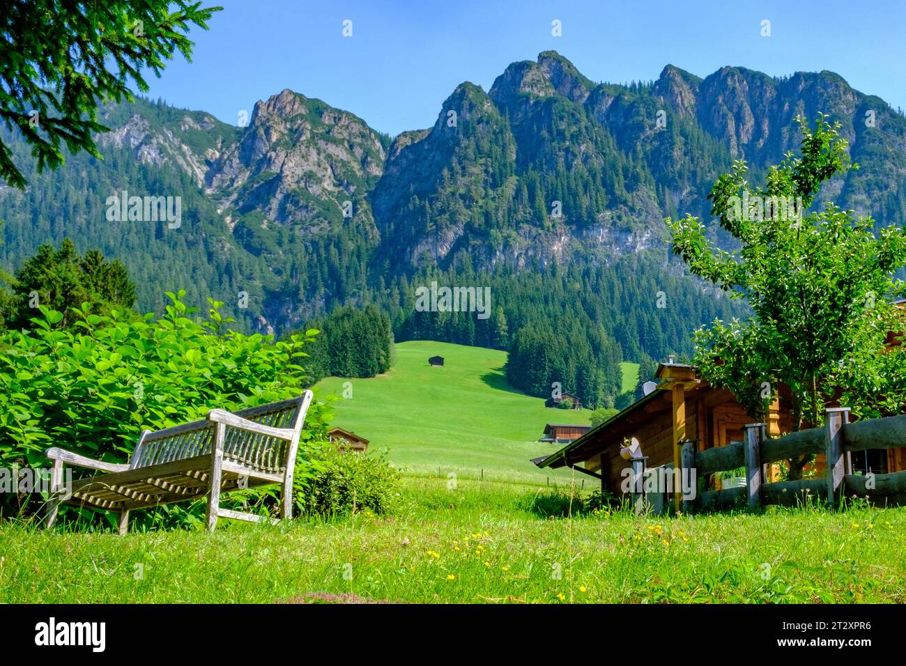 Mountain meadows with a wooden bench. Houses, tall mountain range, blue sky. Alpbach, Austria
