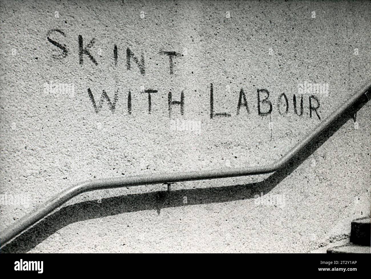 1970s black & white archive photograph of graffiti in Clapham, South London, reads Skint With Labour. Stock Photo