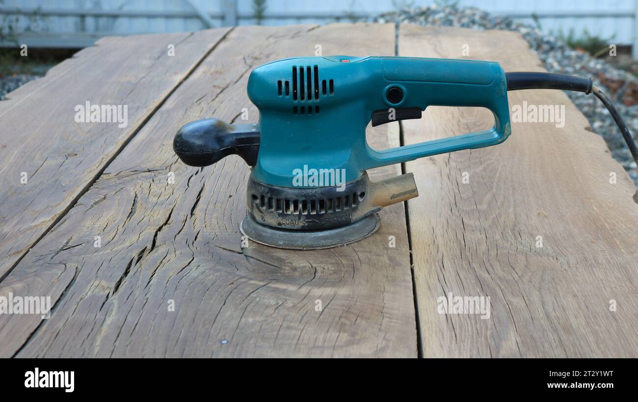 electric sander in a green case standing on the textured surface of solid wooden boards as a