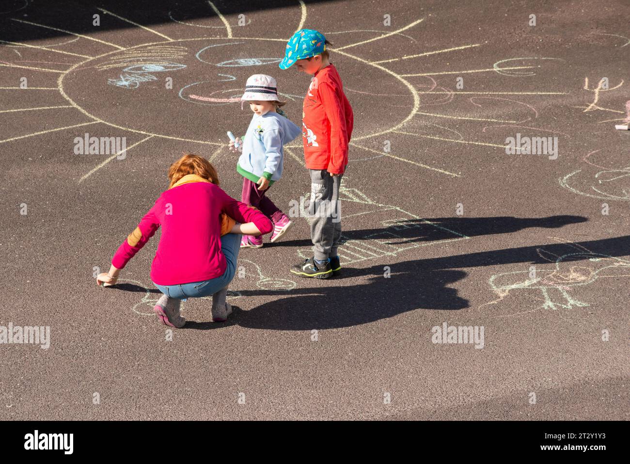 Mother playing with children drawing figures with chalk on asphalt playground as family outdoor activity Stock Photo