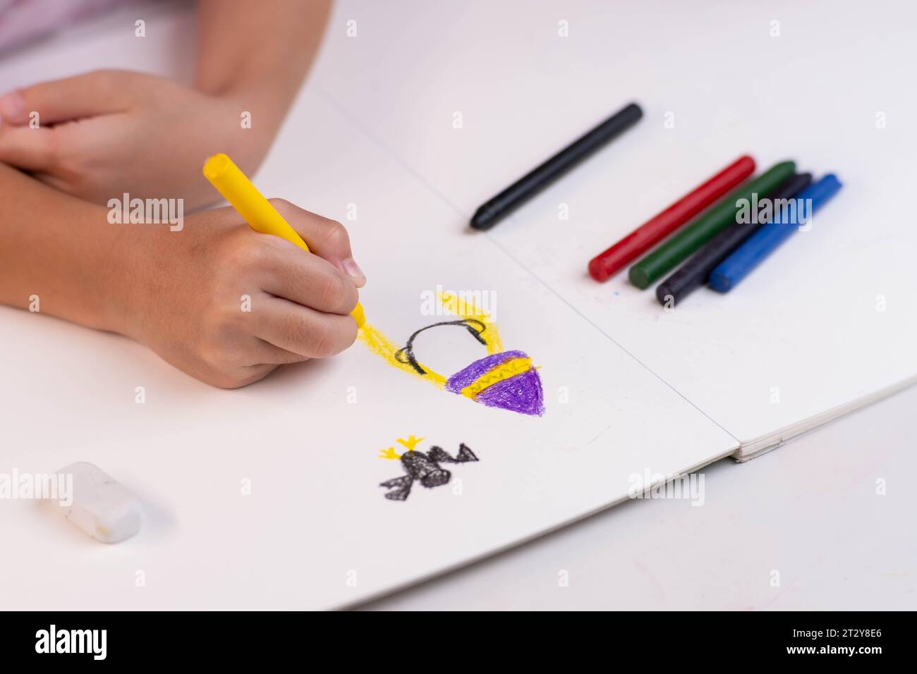 Girl drawing with crayons on a white sheet of paper. Crayons and kids drawing on white background. Close-up of a child's hand holding a crayon and dra Stock Photo