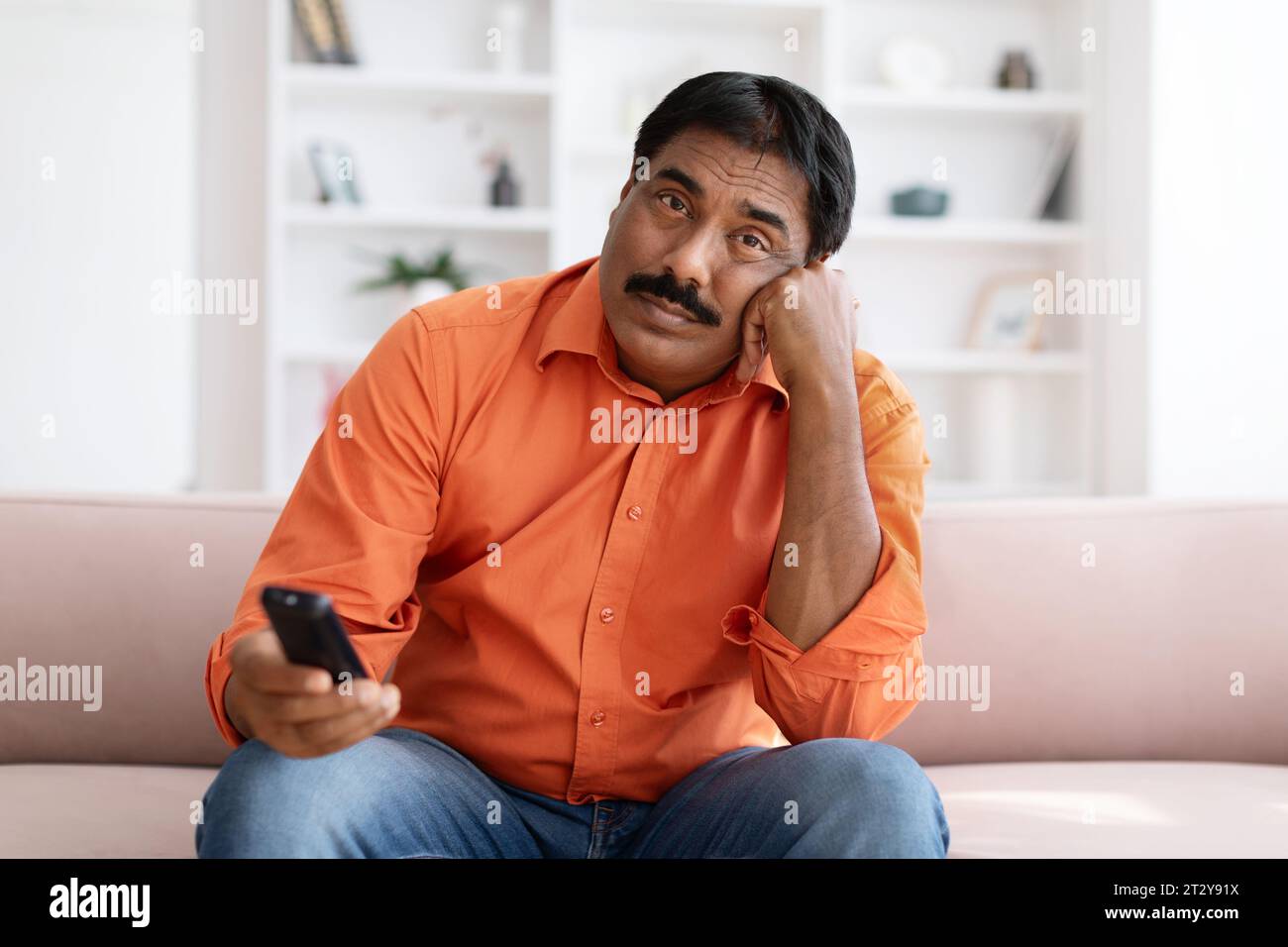Bored Indian Man Watching TV Switching Channels With Remote Control Stock Photo