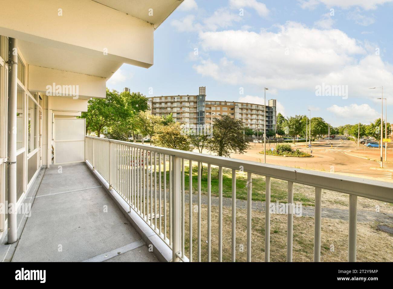 a balcony with white railings and trees in the foregrounded area on the other side of the building Stock Photo