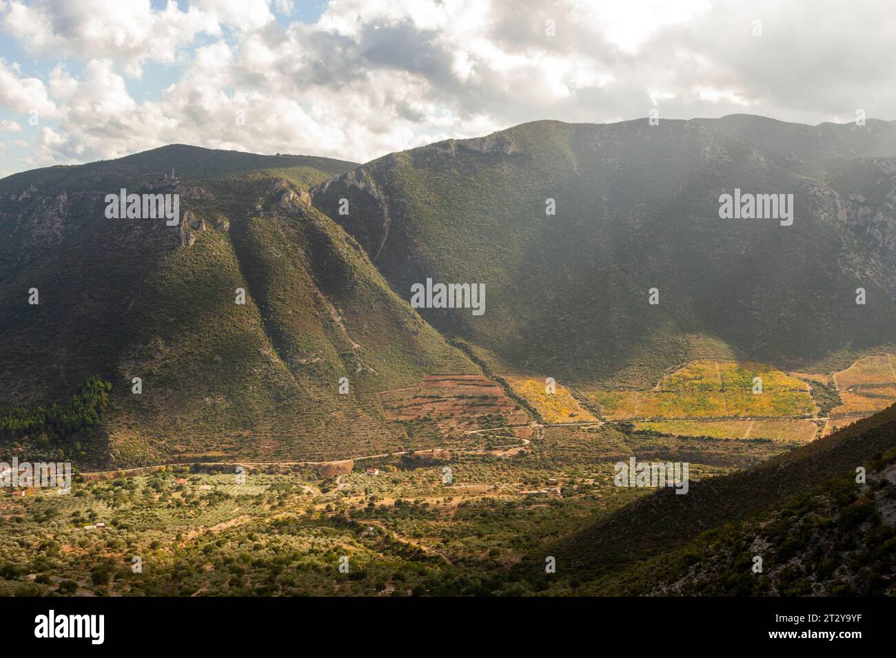 Dreamy landscape with subtle sun rays iluminating the plateau of Leonidio while dark clouds are gathering over the green mountains. Stock Photo