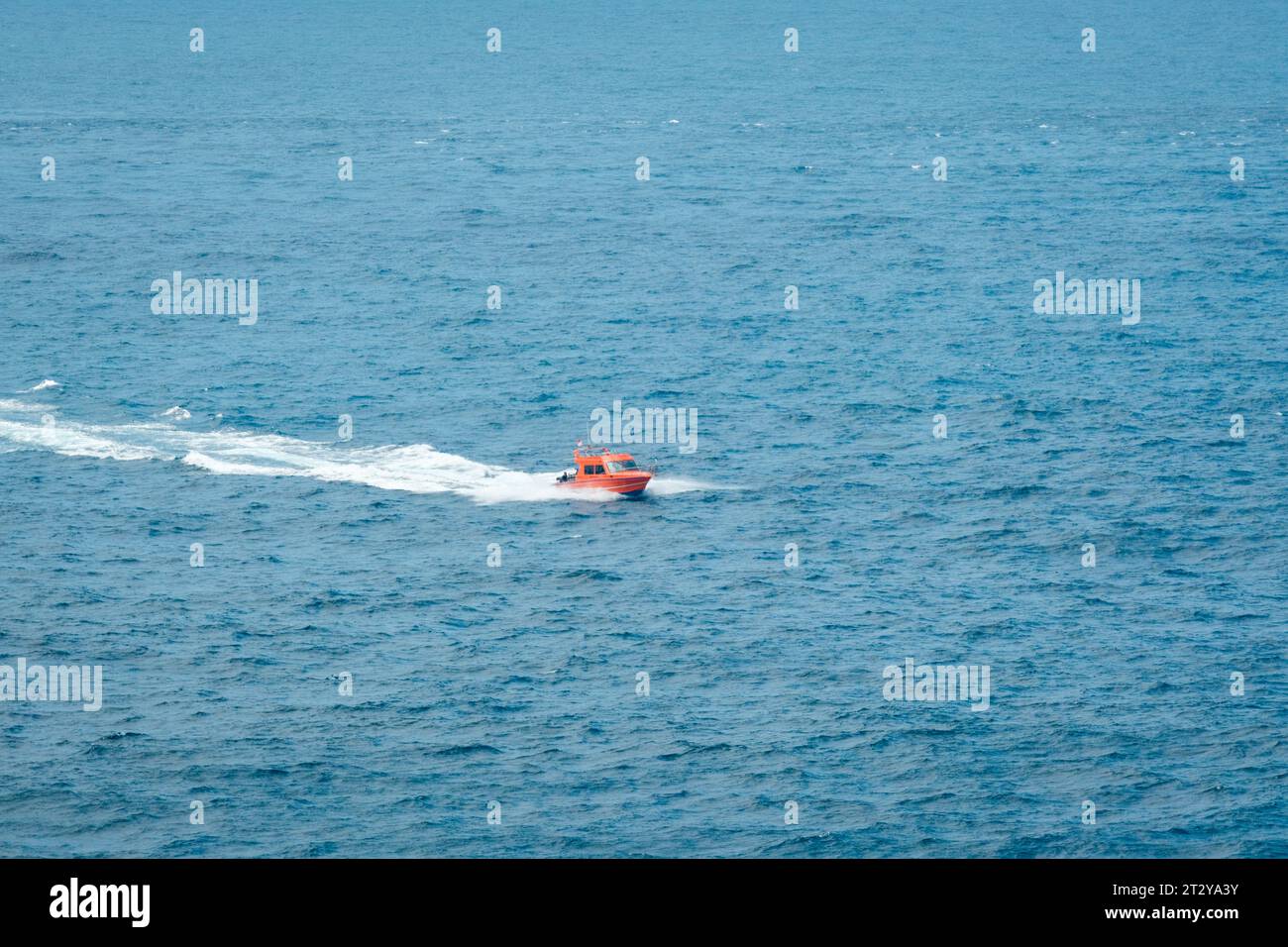 Experience the thrill of speed and the vastness of the open sea as an orange speedboat races across the deep blue waters. Stock Photo
