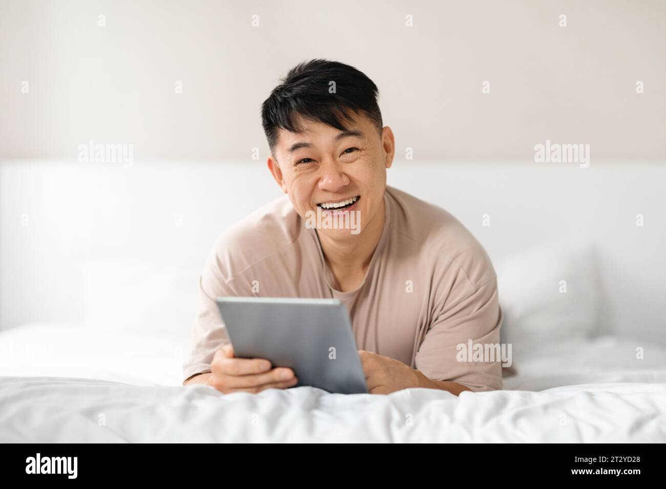 Happy asian man using digital tablet in bed Stock Photo