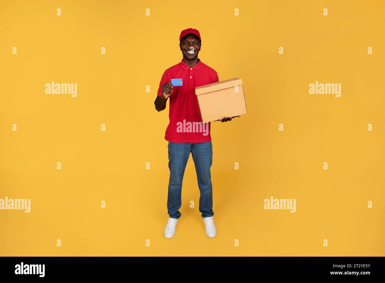 Smiling millennial black guy courier hold box, recommends credit card for pay Stock Photo