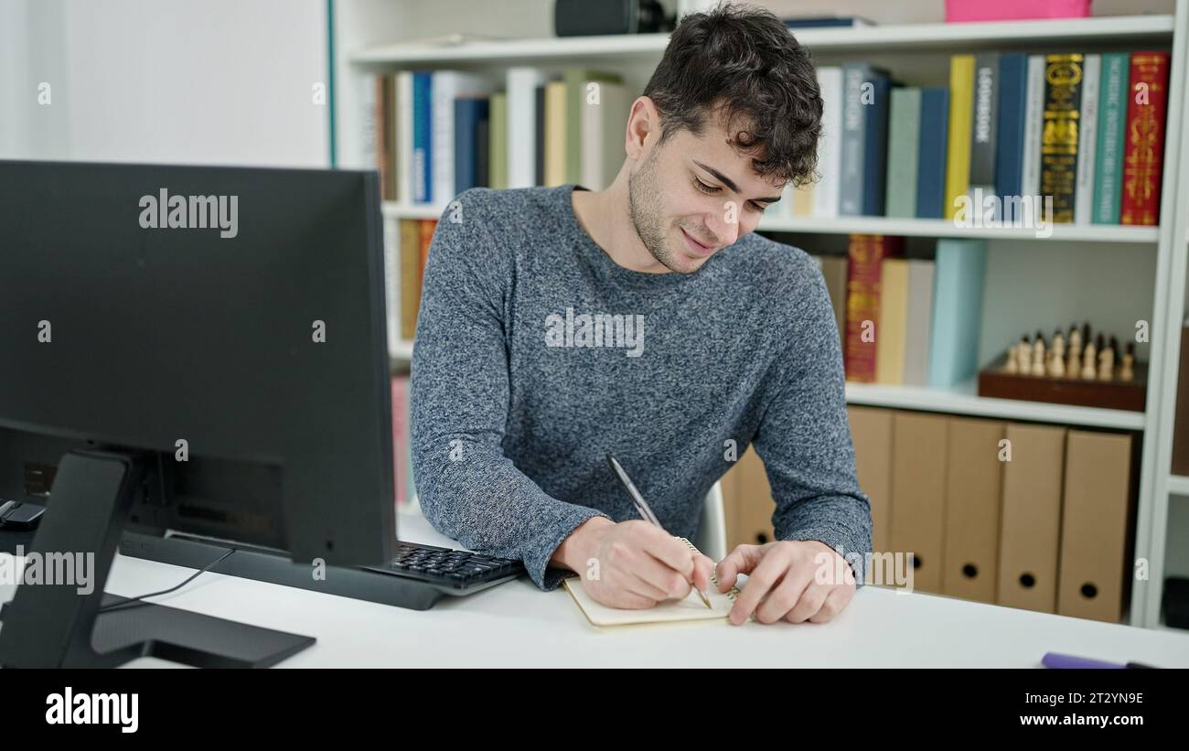 Young hispanic man student using computer taking notes at library ...