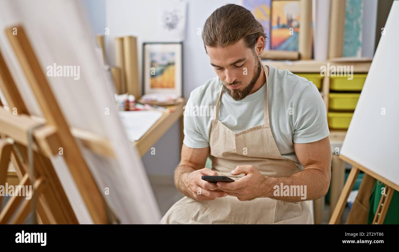 Young hispanic man artist using smartphone at art studio Stock Photo