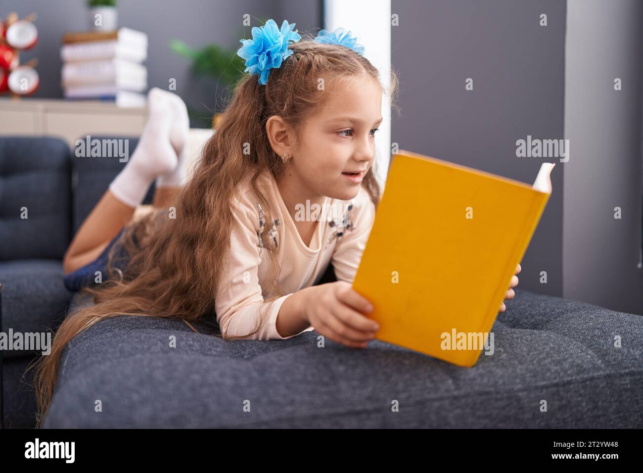 Adorable caucasian girl reading book lying on sofa at home Stock Photo ...