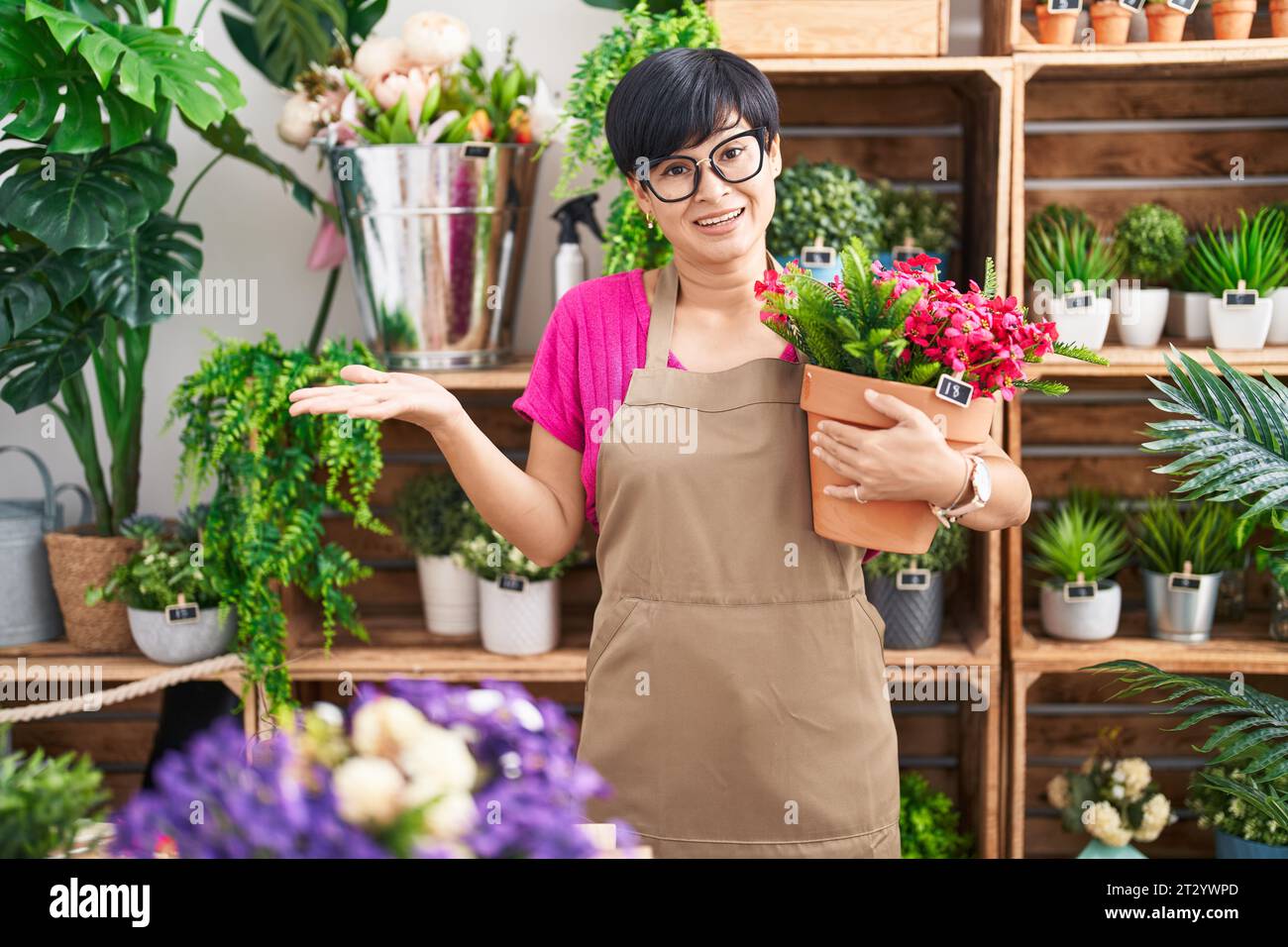 Young asian woman with short hair working at florist shop holding plant ...