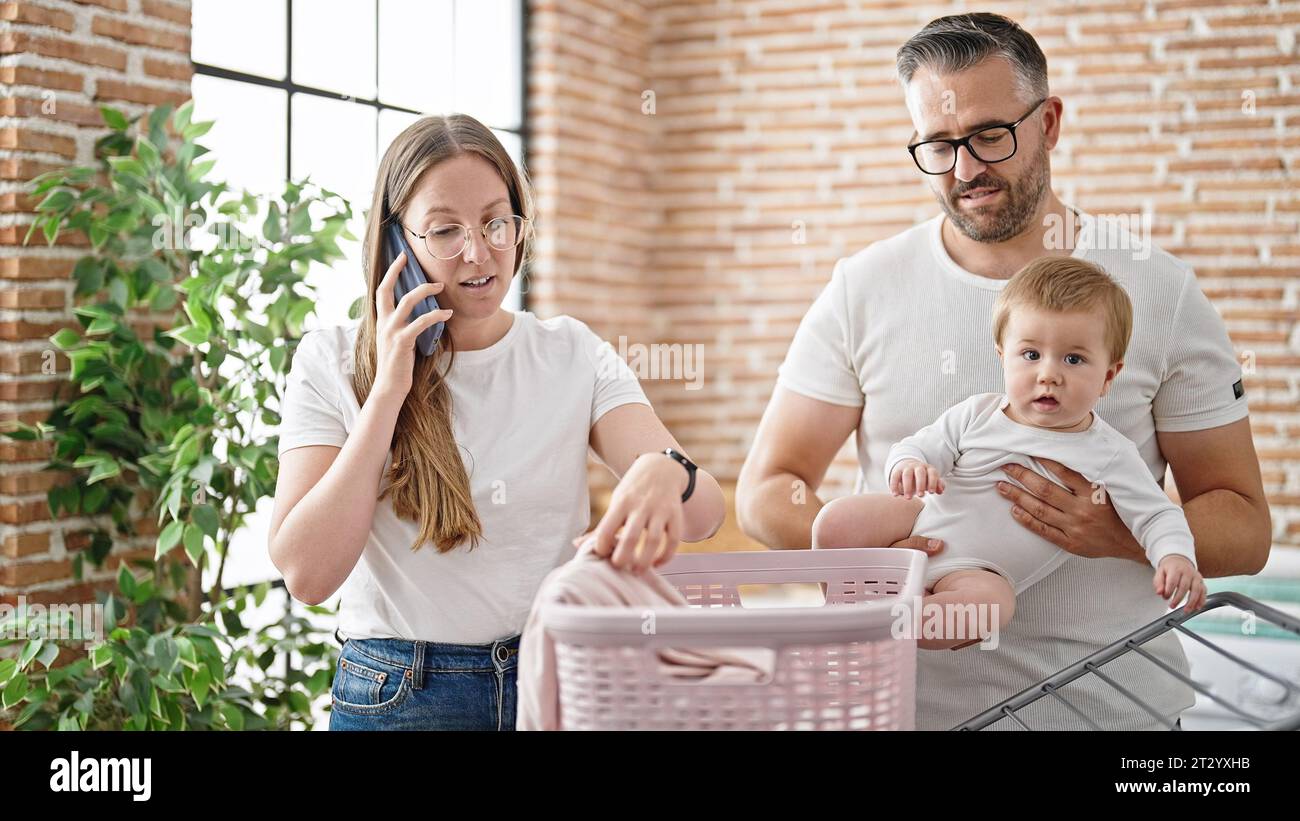 Family of mother, father and baby doing laundry speaking on the phone at laundry room Stock Photo