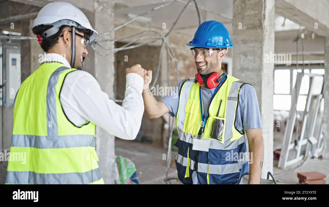 Two men builders smiling confident bumping fists at construction site ...