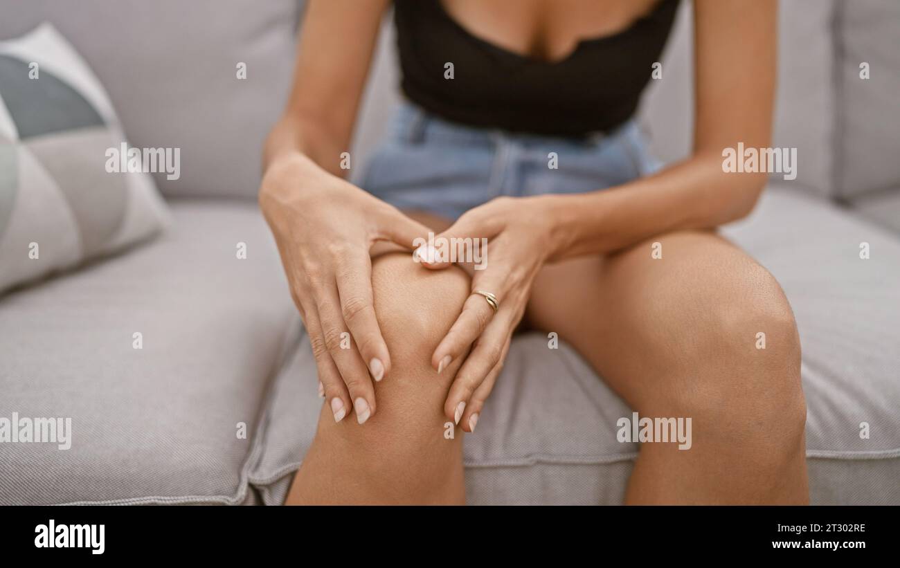 Hispanic adult woman sitting on living room sofa, suffering pain from a ...