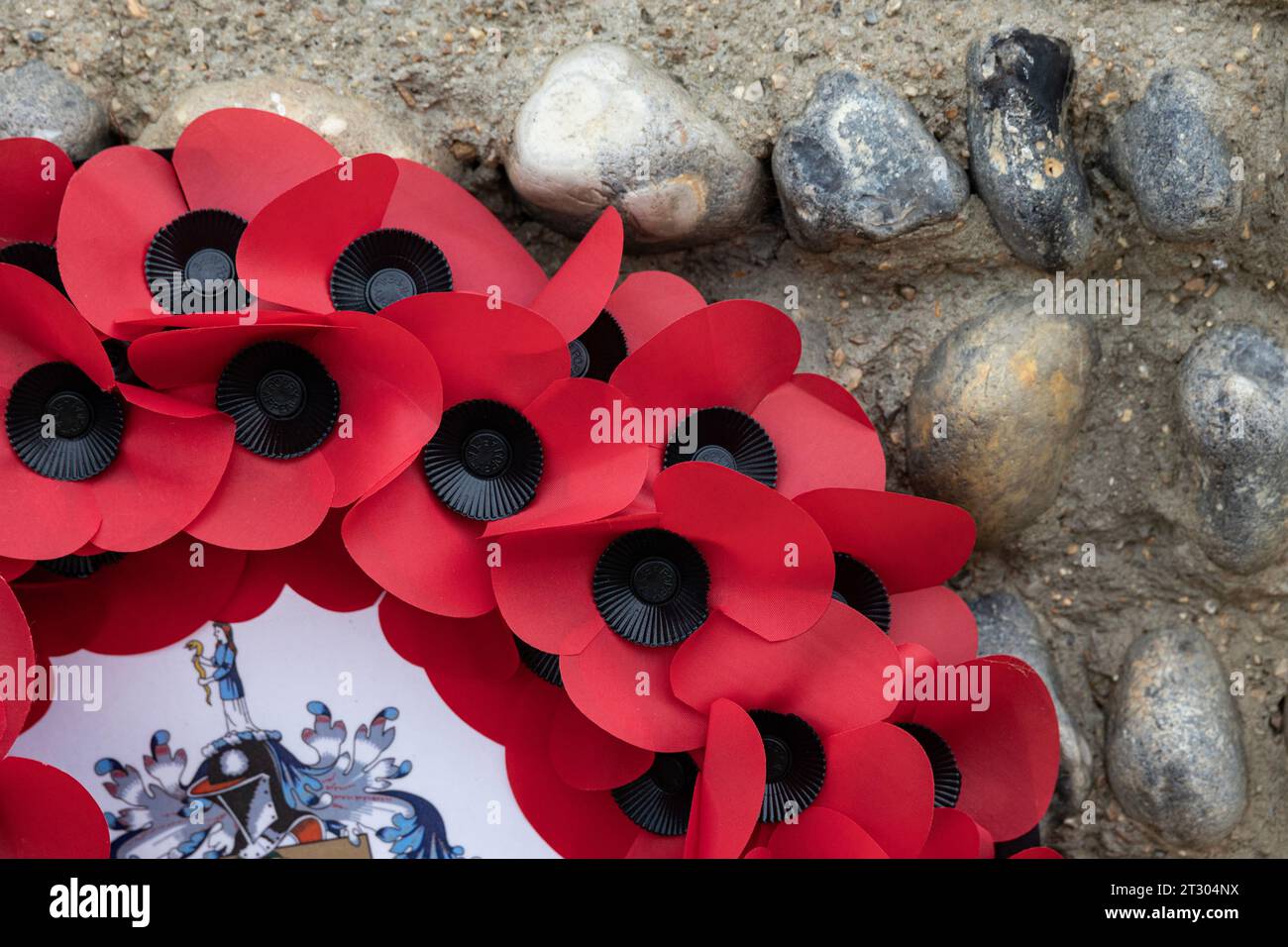 section of a poppy wreath leaning against a flint wall in Worthing, West Sussex, UK Stock Photo
