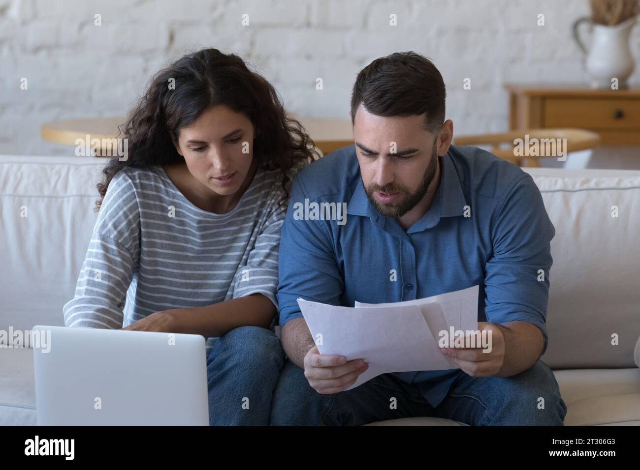 Focused married couple reading paper documents at laptop Stock Photo