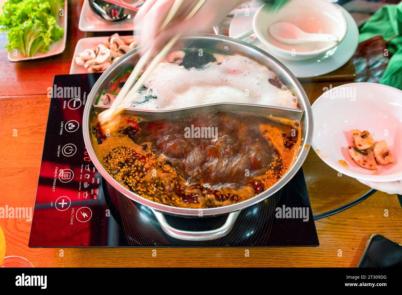 chinese cuisine - adding ingredient in boiling broth in double wok during cooking hotpot soup Stock Photo