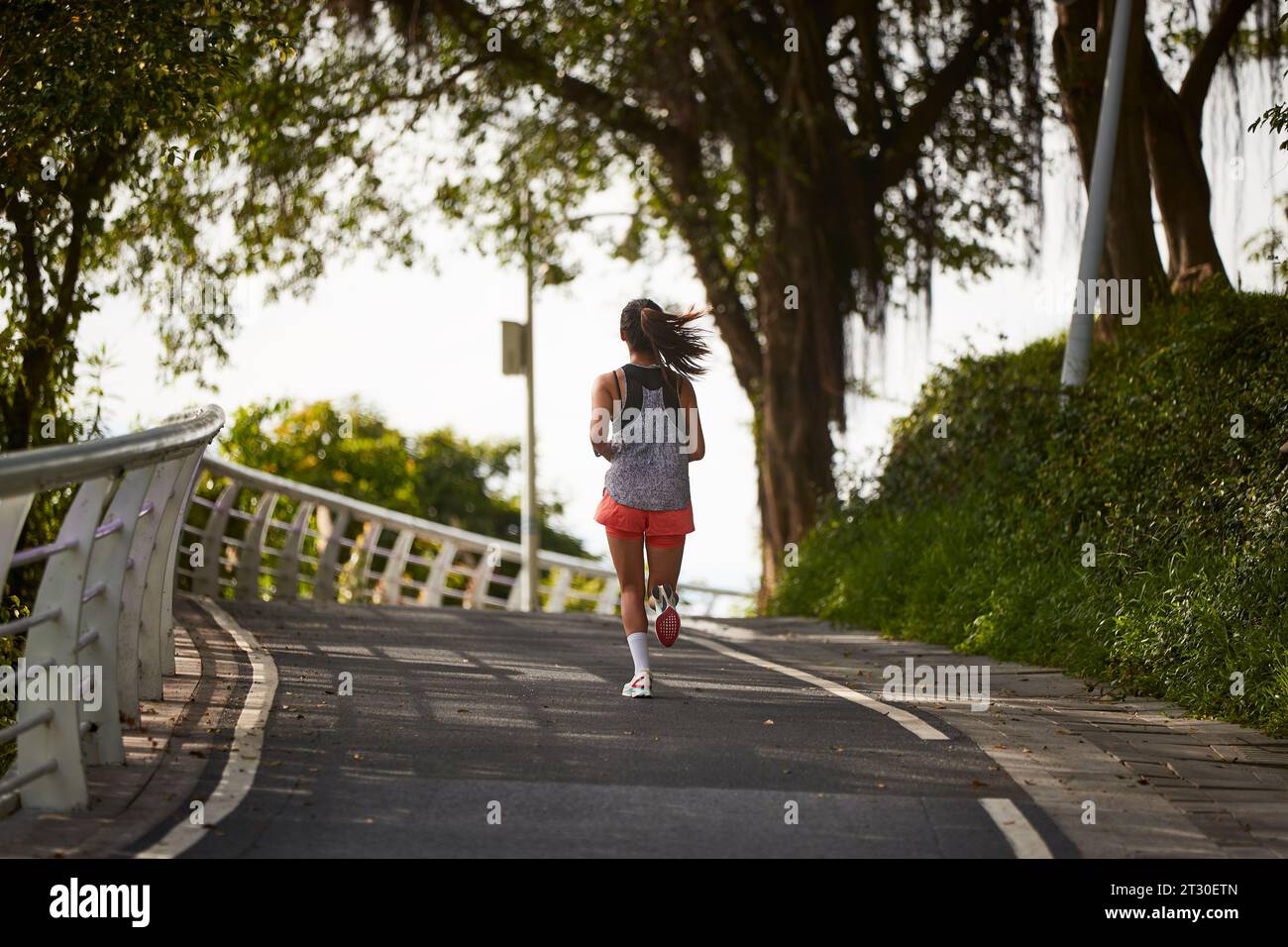 rear view of young asian woman female jogger exercising outdoors in city park Stock Photo