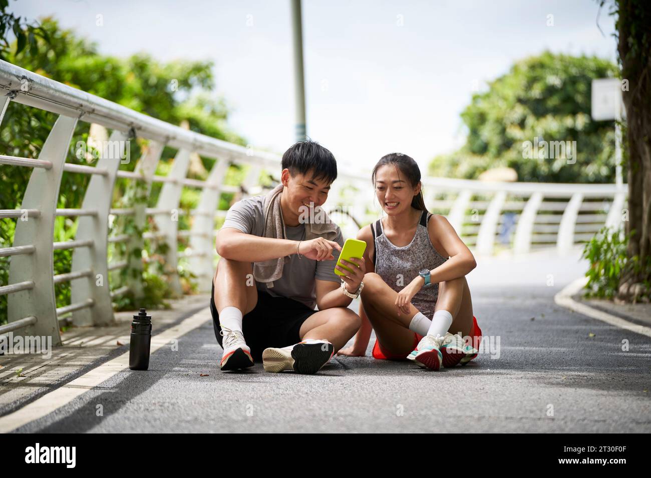 young asian couple looking at cellphone photos while taking a break during outdoor exercise Stock Photo