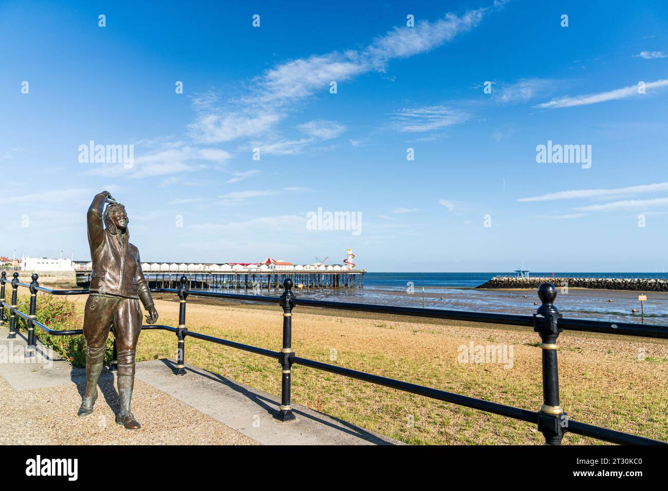 Amy Johnson statue created by Stephen Melton on Herne Bay seafront. Wearing circa 1940's flying costume. Herne Bay pier in the background. Blue sky. Stock Photo