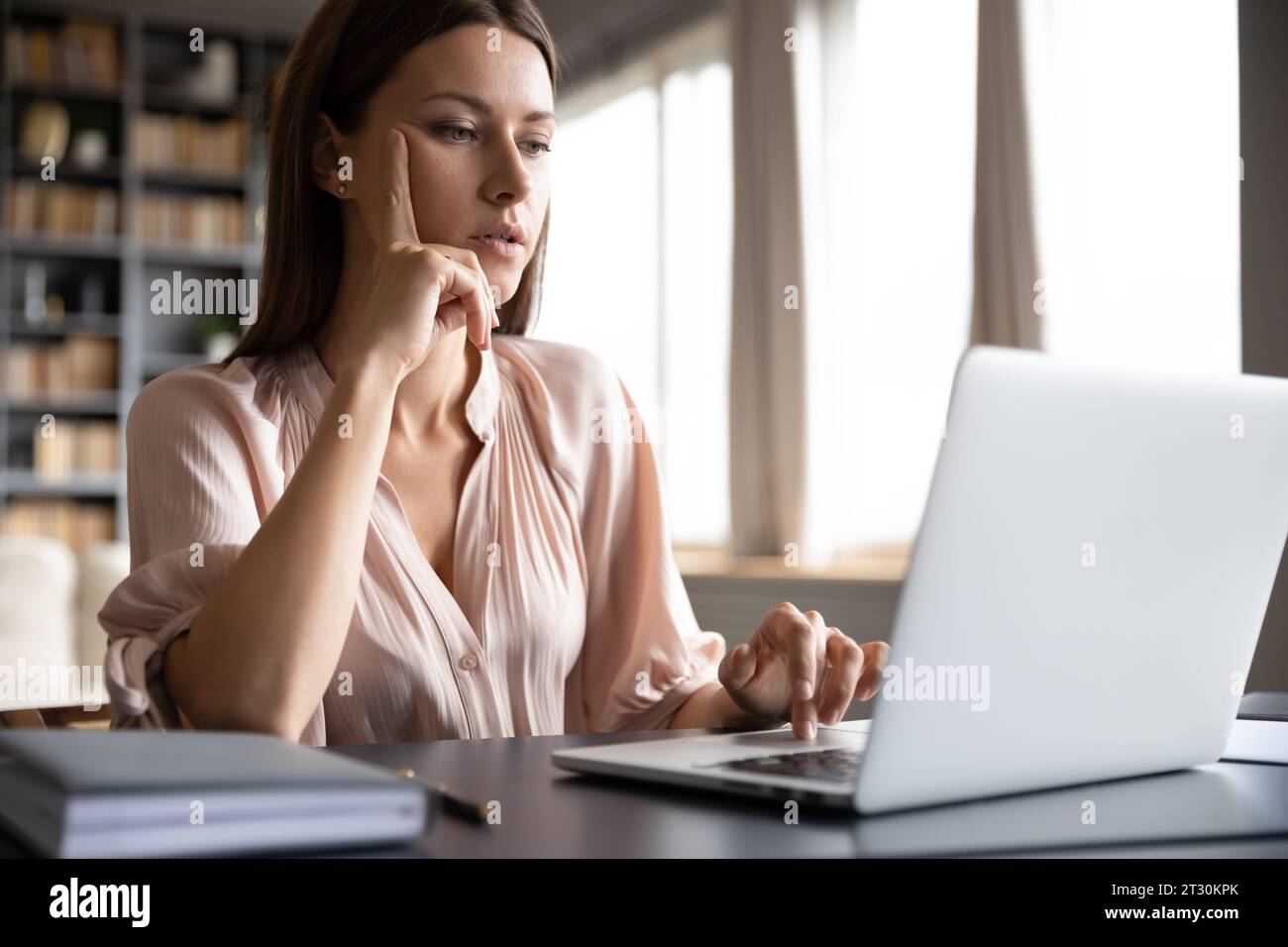 Pensive woman sitting at desk using laptop surfing internet Stock Photo