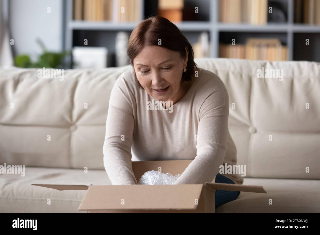 60s woman received parcel enjoy moment of opening box Stock Photo