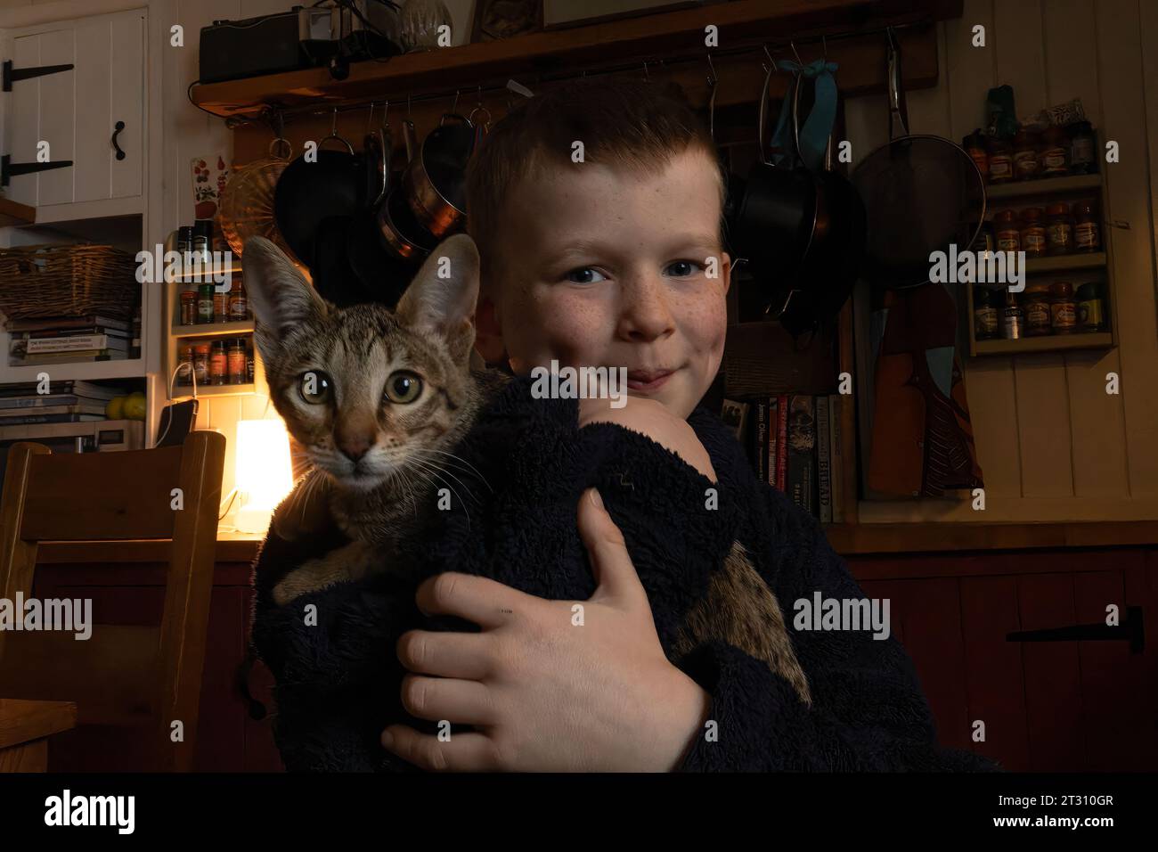 7-year-old boy holding his pet cat (an exotic Savannah breed) at his home in the UK. Stock Photo