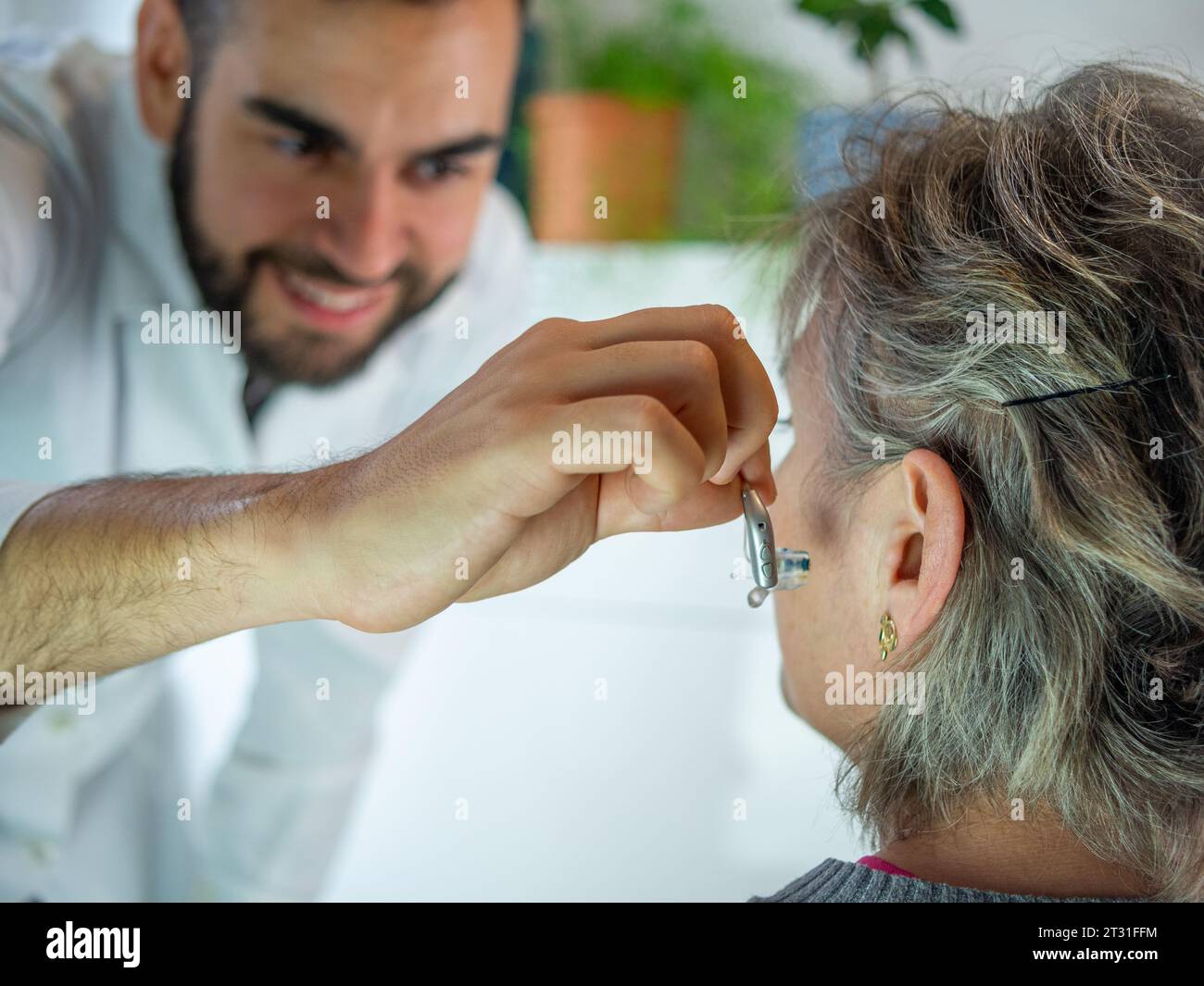 Young male audiologist showing a electronic hearing aid to his patient