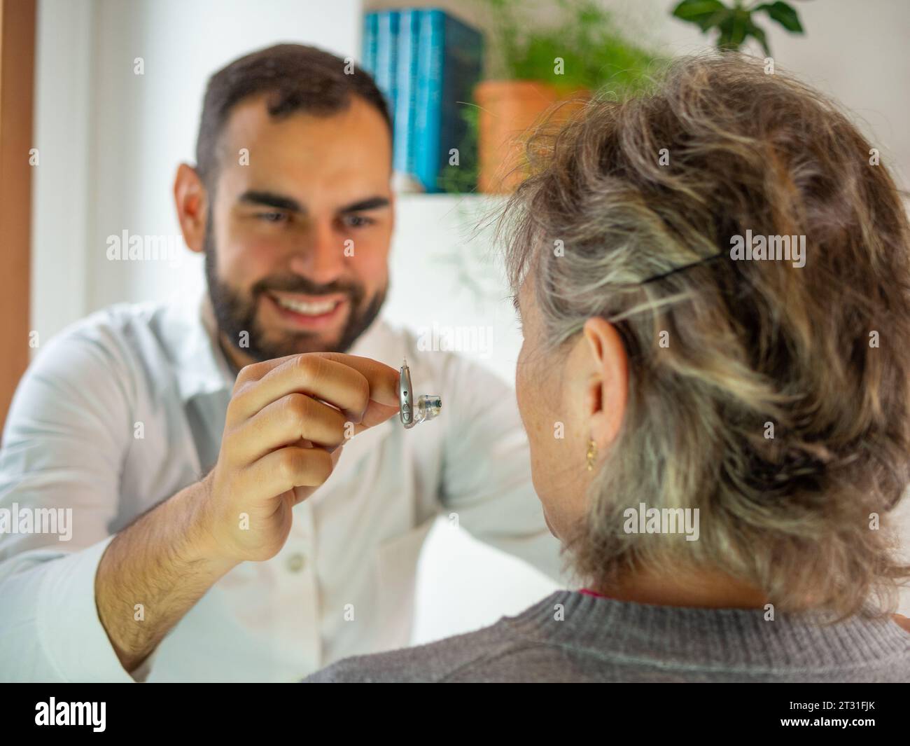 Young male audiologist showing a electronic hearing aid to his patient