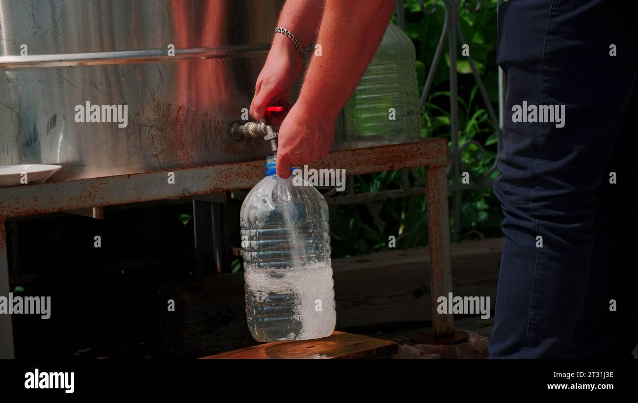 A set of drinking water. Clip. A man with a five-liter bottle draws water from a special column. Stock Photo