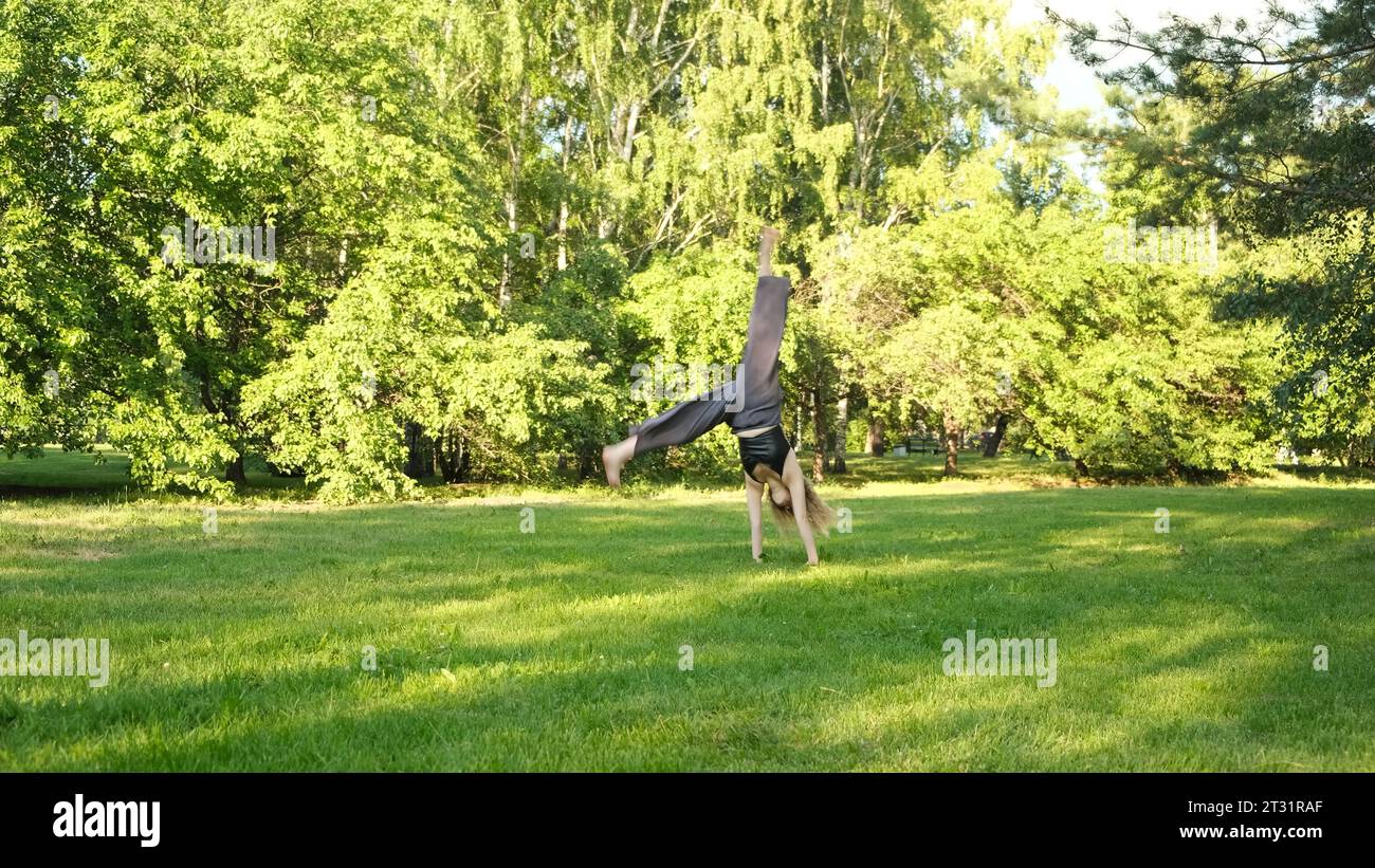 Beautiful woman makes wheel in park in summer. Concept. Young woman ...